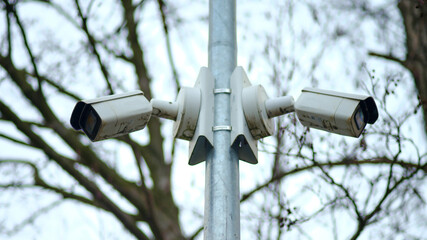 Two white security cameras mounted in opposite directions on a tall metal pole, surrounded by...
