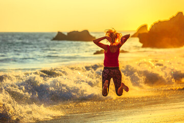 Fototapeta premium Freedom woman jumping on seashore of El Matador Beach at sunset in Malibu Coast, California, United States. Female jumper in California West Coast. Limeston formations on blurred background.