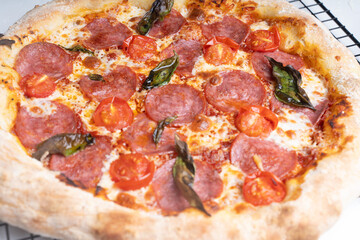 Raw pepperoni pizza is ready to cook. Pizza with sausage, tomatoes, cheese and basil on a baking rack.