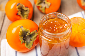 Persimmon jam with slices of ripe persimmon on wooden textured table. Delicious persimmon jam. Marmalade. Healthy sweets. Vegan. Close-up. Space for text. Copy space.