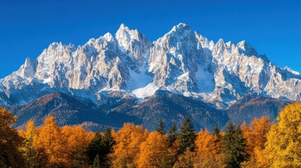 Majestic snow-capped mountains rise against a clear blue sky, surrounded by vibrant autumn foliage, creating a stunning natural landscape.