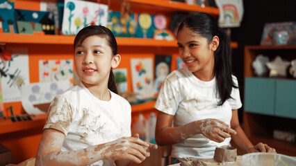 Diverse highschool student modeling cup of clay while wearing dirty shirt at art lesson. Multicultural student working or making dough art in creative activity. Blurring background.. Edification.