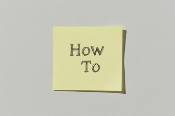 Sticky Note: How To Guide: A simple yellow sticky note with the words "How To" neatly written in dark gray script, ideal for illustrating guides, tutorials, or instructions.  
