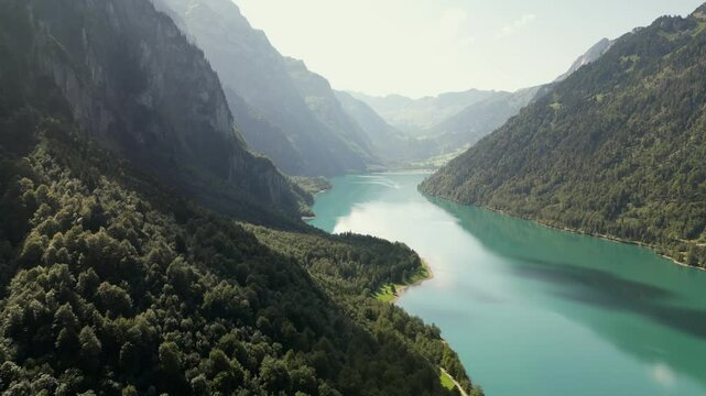 Drone shot of beautiful glacial emerald-green lake surrounded by lush forests,  natural lake in summer afternoon under clear blue sky