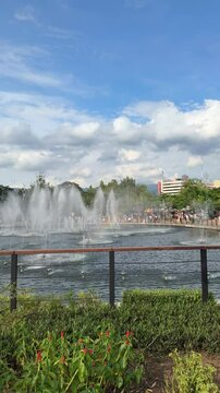 a scenic view of illuminated dancing water fountains  at Kiara Artha Park on a bright sunny day. modern urban park in Bandung with a special show on the lake