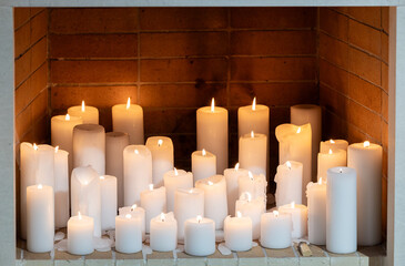 A collection of white candles of varying sizes and burns, arranged in a fireplace. The warm glow of...