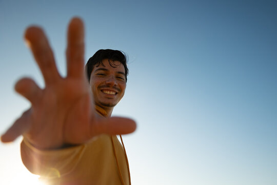 Bottom view of cheerful man reaching hand to camera with blue sky in background on sunny day. Lifestyle