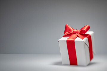 A neatly wrapped white gift box adorned with a vibrant red ribbon is positioned on a clean, gray surface, creating a striking visual. The simple arrangement emphasizes elegance.