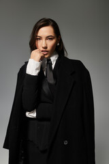 A beautiful young woman showcases her fashion sense in a stylish outfit against a grey backdrop.