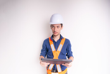 Young architect wearing white helmet and luminous vest, working with laptop. Isolated on white background.