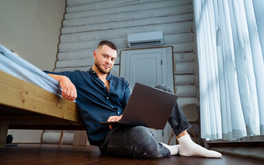 Man working on laptop in cozy room. A man is sitting on the floor of a rustic room, focused on his...