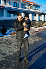 Father carries child on sunny winter day. A father smiles while holding his child in winter clothing on a clear sunny day in a snowy area.