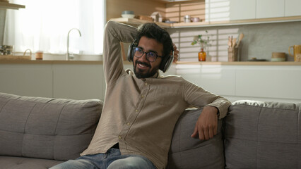 Relaxed Arabian Indian happy hindu man male homeowner relax on cozy sofa comfortable leisure...