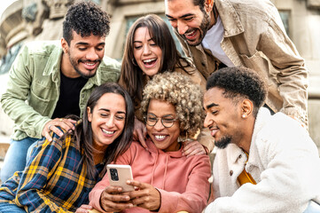 Diverse young people using smart mobile phone device outdoors - Multiracial friends watching smartphone together - Teenagers uploading reel video on social media platform - Youth culture concept .