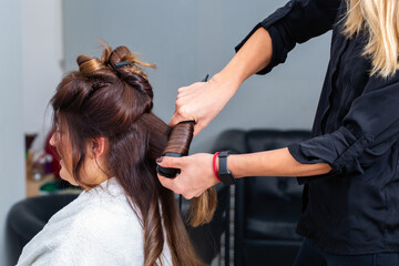 Fototapeta premium Hairdresser making hairdo using curling iron to straighten hair