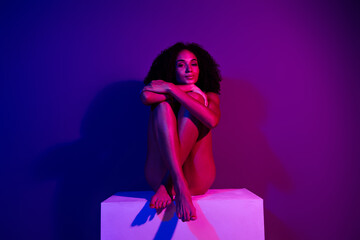 Fashionable young woman posing under purple neon light in a vibrant studio environment