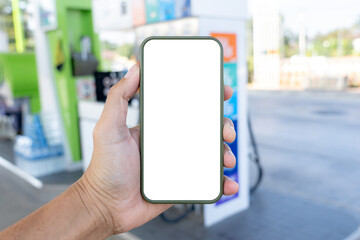 A hand holding a smartphone with a blank screen, with a gas station in the background