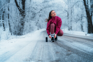 Young athlete tying her shoelaces while preparing for a winter workout in a snowy forest,...