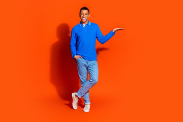 Stylish young man in blue shirt posing against bright orange background
