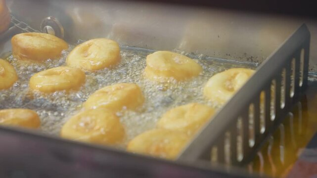 Automated donut production line featuring golden pastries deep frying in bubbling hot oil at industrial bakery manufacturing facility