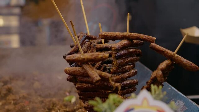 Street food vendor carefully preparing traditional Balkan skewers of cevapcici at bustling outdoor market stall, grilling aromatic meat delicacy