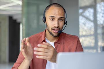 Man with headset and laptop talking using video call, support service worker at workplace inside...
