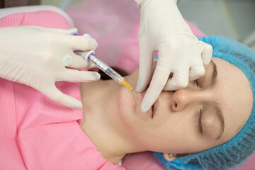 woman is getting filler in lip. The woman is wearing a blue hat and a pink shirt. The woman is...