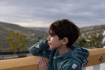 A 9-year-old boy leaning on a balcony on an autumn day contemplating the landscape.