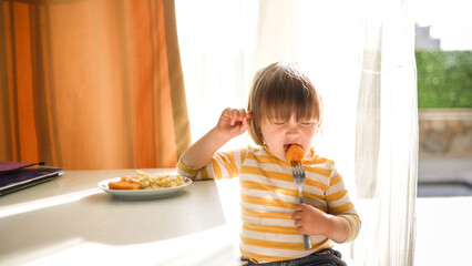 Cute toddler mastering self-feeding with nuggets in a bright, sunny environment.