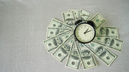 Black alarm clock ticking on one hundred dollar bills displayed in circle shape