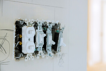 Electrician works on multiple switches, outlets in light filled room of new house under construction.