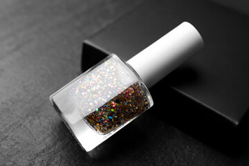 Glitter nail polish in bottle on dark textured table, closeup