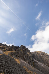 Fototapeta premium Contrail Over Rocky Volcanic Cliff Under Blue Sky