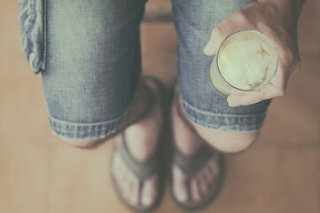 Close-up overhead view of a Man in denim shorts sitting on a chair holding a glass of ice water