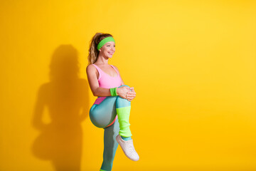 Young sportswoman in vibrant retro sportswear warming up against a bright yellow background, showcasing fitness and style