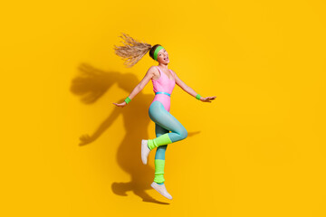 Energetic young woman jumping with joy in vibrant retro activewear against a bright yellow...