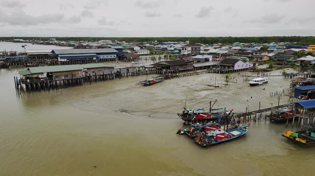 Wooden fishing vessels anchored alongside weathered piers, revealing coastal malaysian settlement's maritime lifestyle under overcast atmospheric conditions