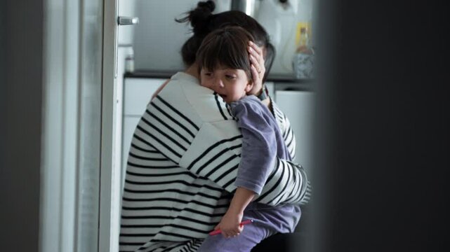 Tender mother consoles son in loving embrace in candid kitchen scene, loving mom with warm embrace of upset crying child struggling with adversity