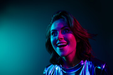 Portrait of stunning young woman look empty space ad wear shiny dress neon light dark blue...