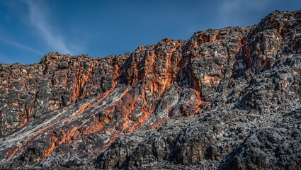Naklejka premium Majestic cliffside with raw iron ore veins under blue sky