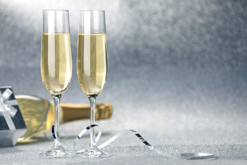 Champagne in glasses, bottle, gift box and streamers on silver background. Space for text