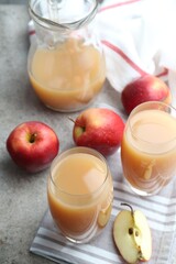Refreshing apple juice in glasses and fruits on grey textured table