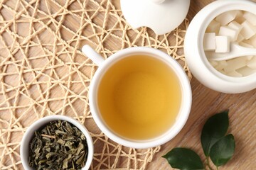 Refreshing green tea in cup, sugar bowl and leaves on wooden table, flat lay