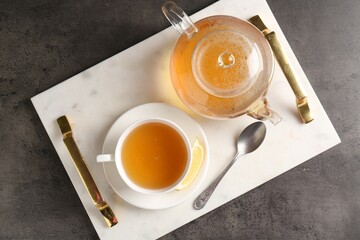 Refreshing green tea, spoon and slice of lemon served on dark textured table, top view