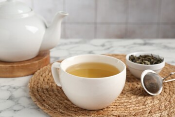 Refreshing green tea, strainer and dry leaves on white marble table, closeup