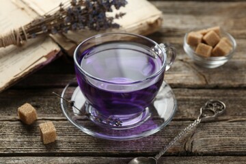 Aromatic lavender tea in glass cup, brown sugar, book, spoon and bunch of dry flowers on wooden...