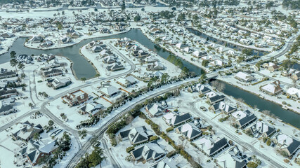 Aerial views of a snow-covered suburban neighborhood with houses, roads, ponds, and recreational facilities.
