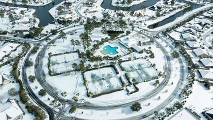 Aerial views of a snow-covered suburban neighborhood with houses, roads, ponds, and recreational facilities.