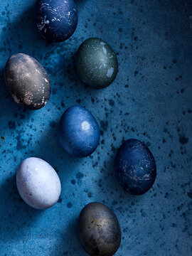 A collection of beautifully dyed eggs in various shades of blue and green is placed on a textured blue surface, creating a festive atmosphere for a spring event