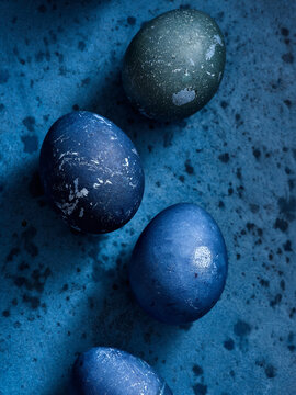 Vibrant easter eggs in various shades of blue and green are arranged on a richly colored blue surface, highlighting the creativity of seasonal festivities